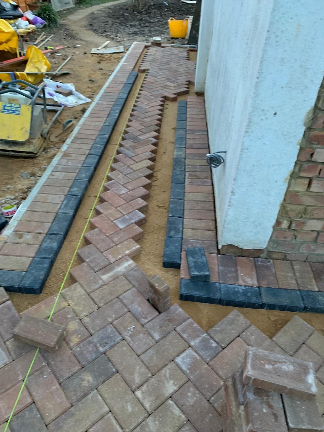 Block paving being laid with charcoal soldier course borders against a rendered wall