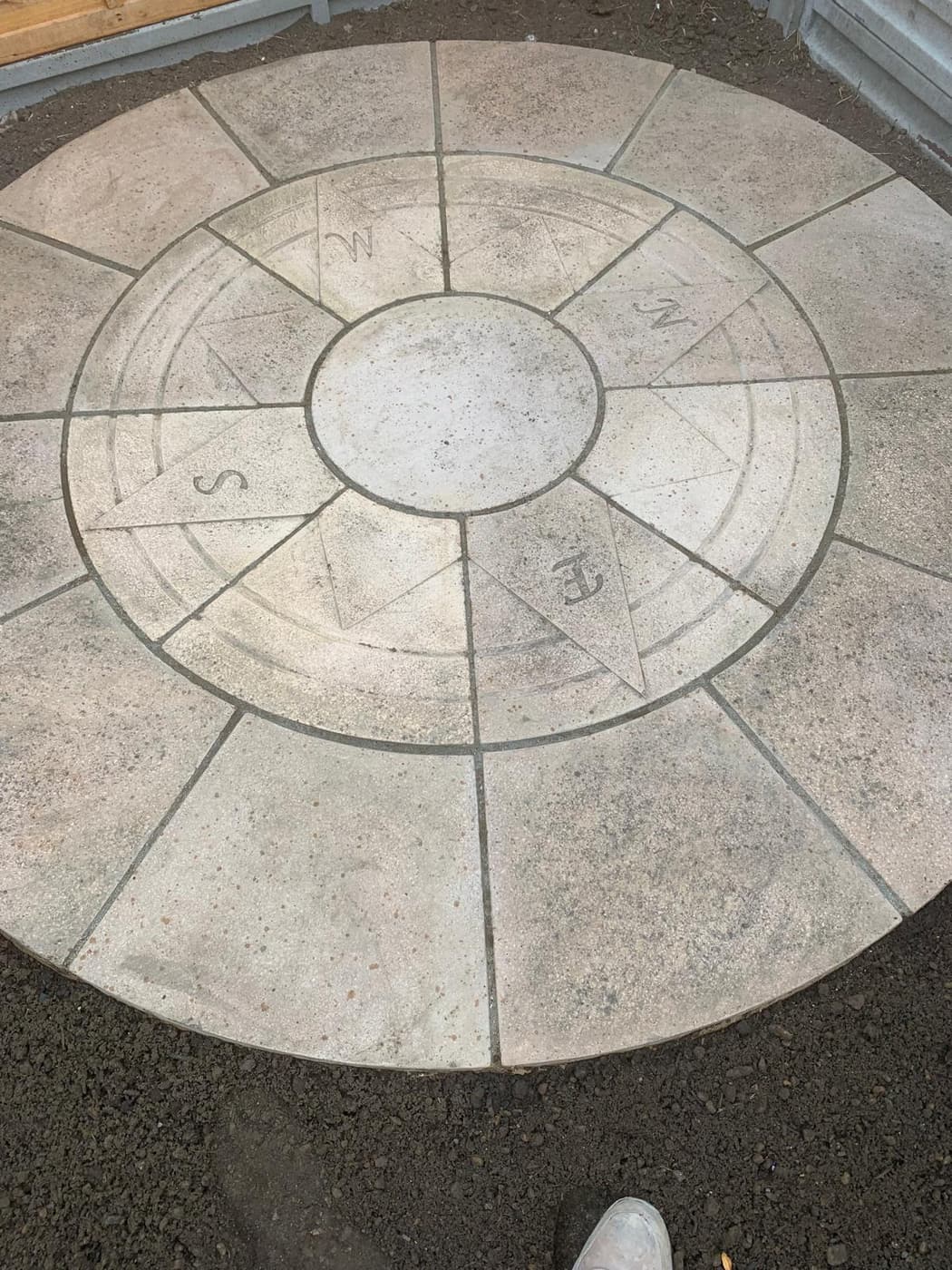 Circular paving feature with a compass rose centre being set out on a bed of soil