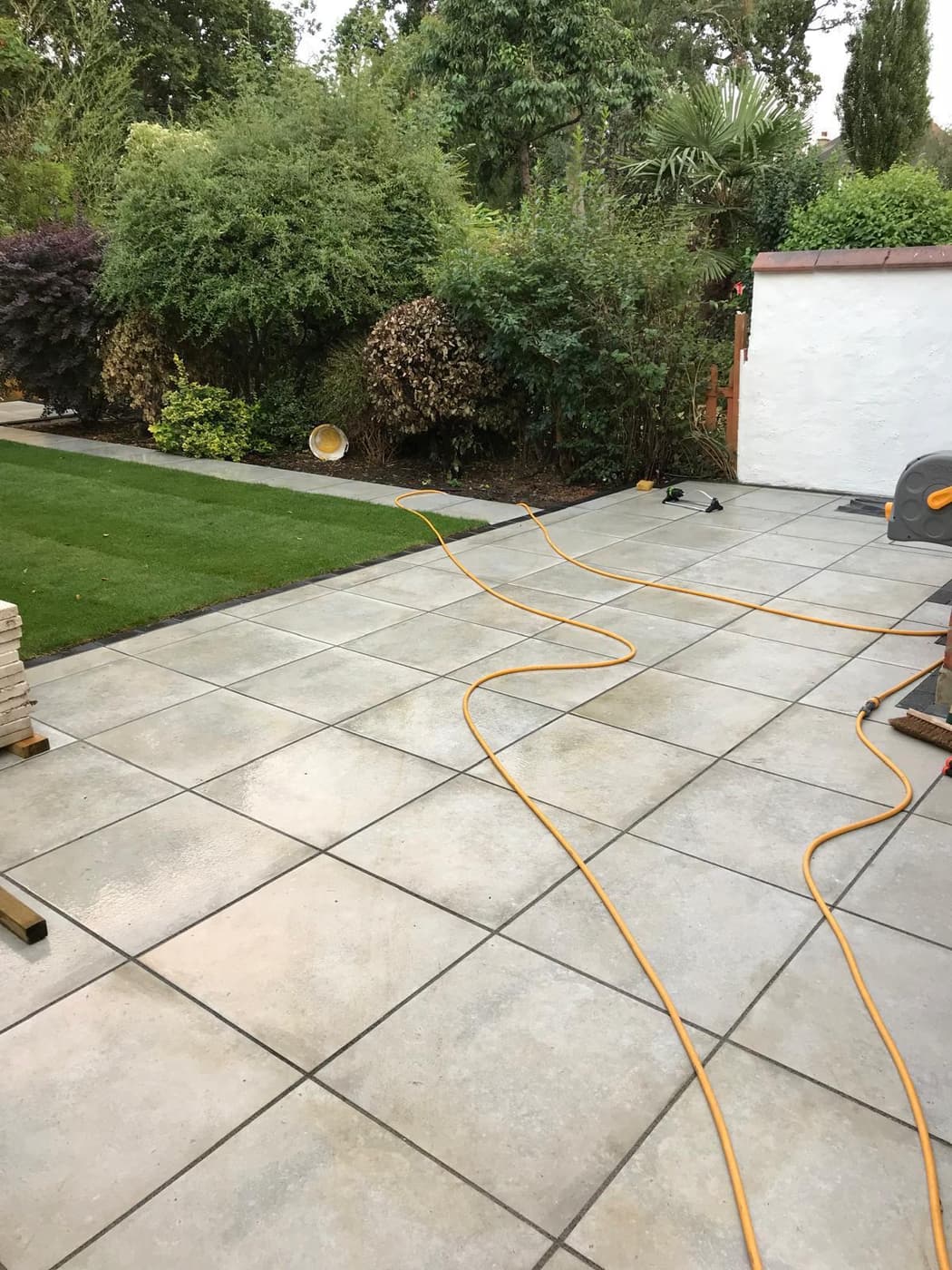 Large-format grey porcelain patio slabs laid alongside a mown lawn and planted border